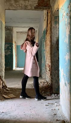 a woman in a pink sweater and black leggings standing in an old building