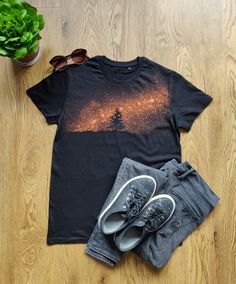 a t - shirt, pair of shorts and sunglasses on a wooden floor next to a potted plant