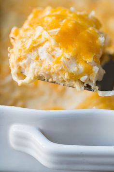 a spoon full of cheesy potato casserole being lifted from the casserole dish