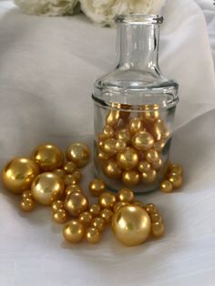 a glass bottle filled with gold pearls next to a white rose on a tablecloth