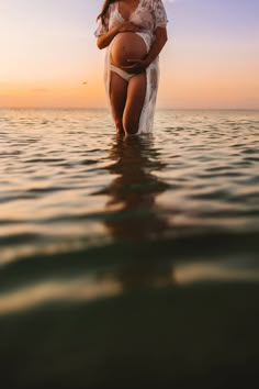 a pregnant woman standing in the ocean at sunset with her belly wrapped around her waist