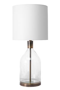 a clear glass lamp with a white shade on the base and a gold metal base