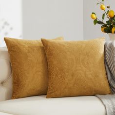 two pillows sitting on top of a couch next to a vase filled with yellow flowers