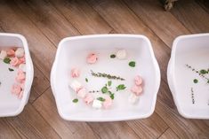 three white bowls filled with flowers on top of a wooden floor next to each other