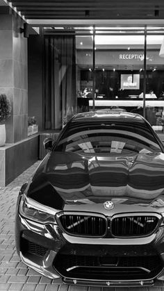 a black and white photo of a car parked in front of a retail store with its hood up