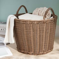 a wicker laundry basket with white towels in it on a wooden floor next to books