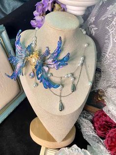 Dive into a world of enchantment with our Ethereal Mermaid Fairy Wing Choker. This stunning piece embodies the magic where sea meets sky, blending the allure of mermaids with the whimsy of fairies. Key Features: * Handcrafted iridescent wings that shimmer with every movement * Mesmerizing blue and purple hues reminiscent of twilight over calm seas * Unique asymmetrical design featuring a delicate gold-toned centerpiece * Choker style for a close, elegant fit Artisan Craftsmanship: Each wing is a Ethereal Mermaid, Ethereal Fairy, Iridescent Wings, Fantasy Necklace, Magical Accessories, Mermaid Fairy, Iridescent Blue, Wing Necklace, Unusual Jewelry