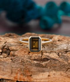 a yellow gold ring with a green tourmaline stone in the center on top of a piece of wood