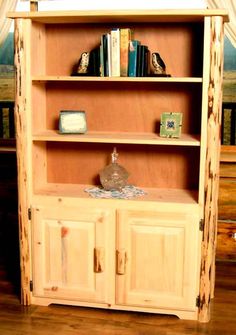 a wooden bookcase with two doors and shelves on the top, in front of a painting