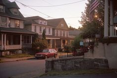 a red car parked on the side of a road next to some houses and an american flag