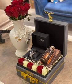 a white vase with red roses in it next to a watch and other items on a table