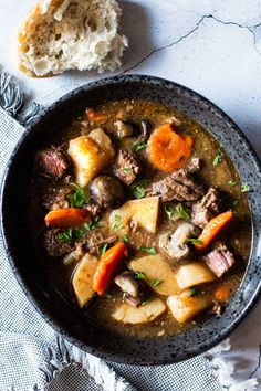 a bowl filled with stew next to a piece of bread on top of a table