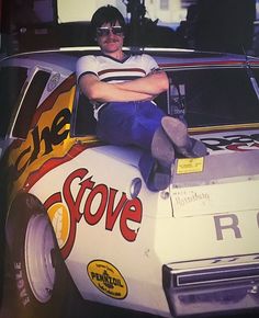 a man sitting on the hood of a race car with his arms crossed and legs crossed