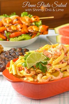 a bowl of pasta with shrimp and lime garnish next to grilled meat