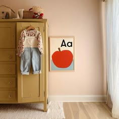 a baby's room with an apple poster on the wall and clothes hanging up