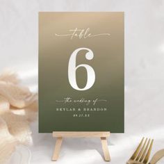 a table number card with the number six on it next to a fork and napkin