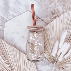 a glass jar with a straw inside sitting on top of some white feathers and an umbrella