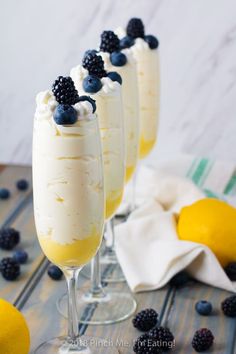 three glasses filled with ice cream and topped with blueberries, lemons and blackberries