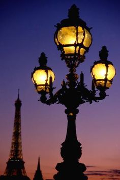 the eiffel tower is lit up at night, with street lamps in front