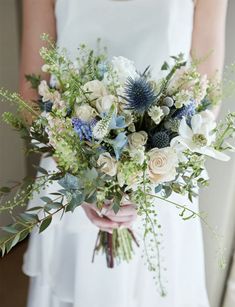 a bridal holding a bouquet of white and blue flowers with greenery on it