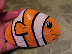 an orange and white clown fish toy being held by someone's hand on a bed