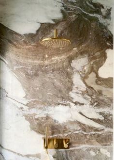 an image of a bathroom setting with marble and brass fixtures on the wall, including two faucets