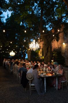 a group of people sitting around a table at a dinner under a tree with lights