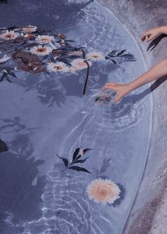 a woman is in the water with her hands out and flowers floating on top of it