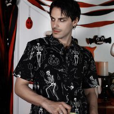 a man with black hair wearing a skeleton shirt and holding a bottle in his hand