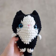 a crocheted black and white cat with blue eyes is held up to the camera