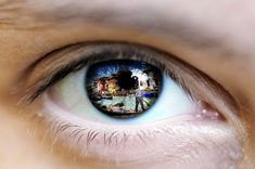 a person's eye with the reflection of a city in their blue iris lens