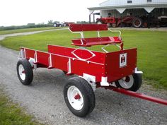 a red wagon sitting on top of a gravel road next to a green grass covered field