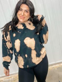 a woman with black hair wearing a green and brown sweatshirt, leggings and gold hoop earrings