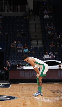 a man standing on top of a basketball court with his foot in the air while wearing green and white shoes