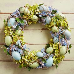 an easter wreath with blue and green eggs, greenery and flowers on a white wooden background