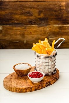 french fries and ketchup on a wooden cutting board next to a bowl of ketchup