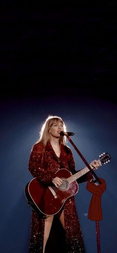 a woman in a red dress holding a guitar and singing into a microphone on stage