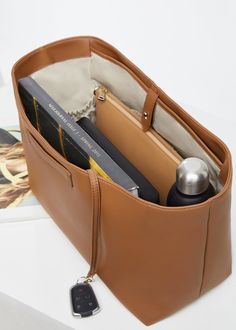 a tan leather purse with books and other items in it on top of a table