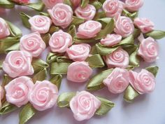 small pink flowers with green leaves on a white tablecloth, ready to be made into brooches