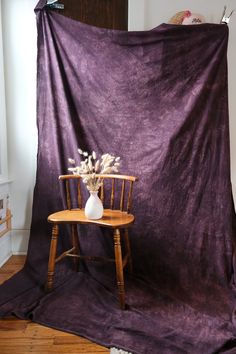 a chair with a vase on it in front of a purple cloth draped over it