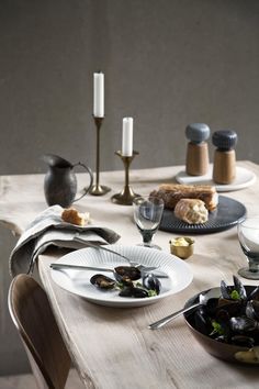 a wooden table topped with plates and bowls filled with mussels next to candles