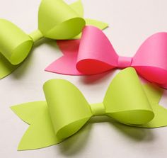 three pink and green paper bows on a white surface