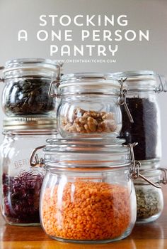 four glass jars filled with different types of food on top of a wooden table and text overlay reading stocking a one person pantry