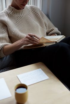 a woman sitting on a couch reading a book with a cup of coffee next to her