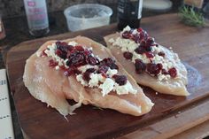 two pieces of fish with cranberries and cheese on them sitting on a cutting board