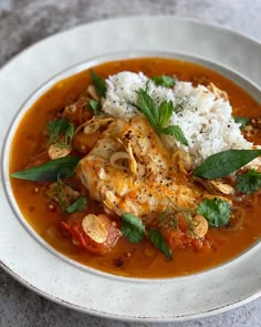 a white plate topped with meat and vegetables covered in sauce, garnished with herbs