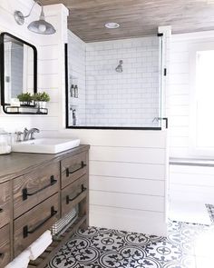 a white bathroom with black and white tile flooring, wooden vanity, and shower