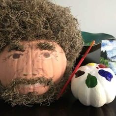 a man's face is covered in grass next to a pumpkin and painting supplies