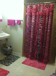 a zebra print shower curtain in a bathroom with pink rugs and towels on the wall