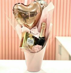 a pink vase filled with champagne, balloons and heart shaped gold foil balloon in front of a pink wall